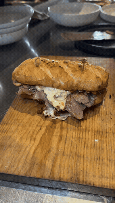 A Sandwich Is On A Wooden Cutting Board On A Table GIF