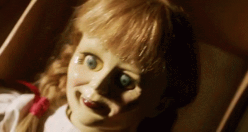 A Scary Doll Is Laying In A Box And Smiling At The Camera . GIF