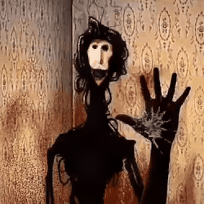 A Scary Doll Is Standing In Front Of A Wall With A Hand Reaching Out . GIF