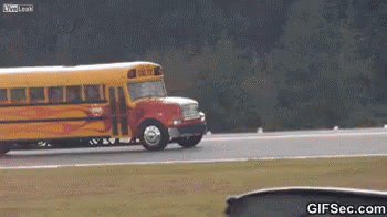 A School Bus Is Driving Down A Road With Flames Coming Out Of The Wheels GIF