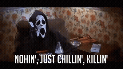 A Scream Masked Person Is Sitting On A Couch Talking On A Cell Phone .. GIF