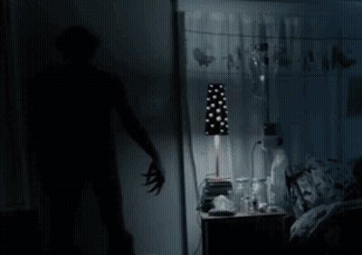 A Shadow Of A Person Standing In A Dark Room With A Lamp GIF