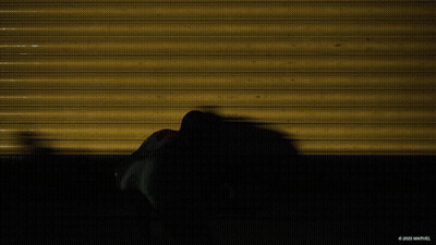 A Shadow Of A Spider Man Is Cast On A Yellow Wall With The Marvel Logo In The Corner GIF