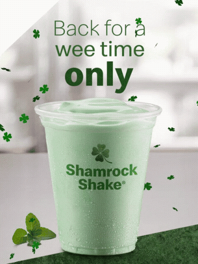 A Shamrock Shake In A Plastic Cup With Shamrocks Around It GIF