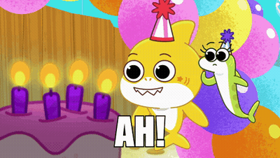 a shark wearing a party hat stands next to a cake with candles