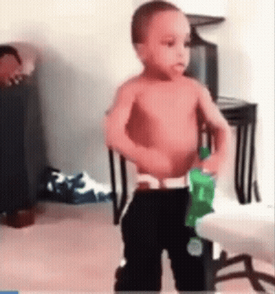 A Shirtless Baby Is Holding A Green Bottle Of Soda . GIF