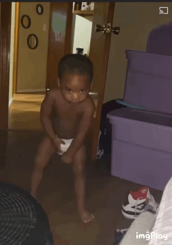 A Shirtless Baby Is Standing In A Room With A Purple Container In The Background GIF