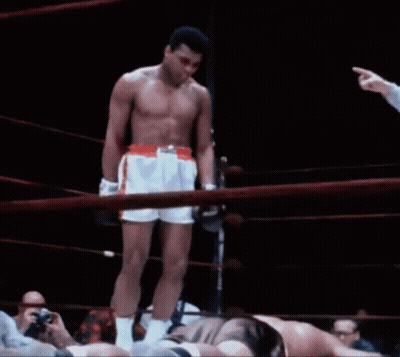A Shirtless Boxer Stands In The Middle Of A Boxing Ring While A Referee Points At Him GIF