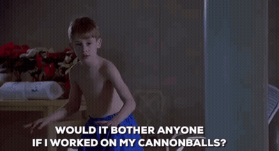 A Shirtless Boy In Blue Shorts Is Standing In A Dark Room And Talking To Someone . GIF