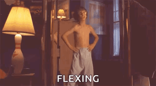 A Shirtless Boy Is Standing In A Room With His Hands On His Hips And The Word Flexing Written On The Screen . GIF