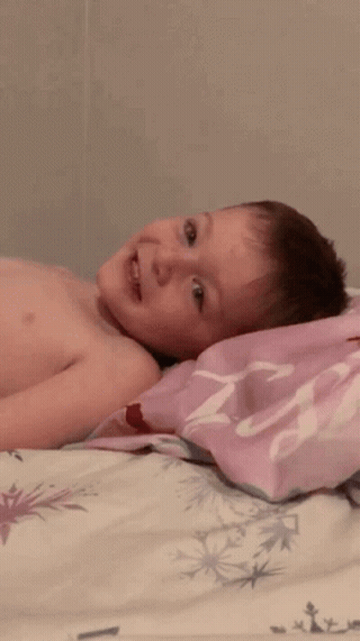 A Shirtless Child Is Laying On A Bed With A Pink Pillow That Says ' Princess ' On It GIF