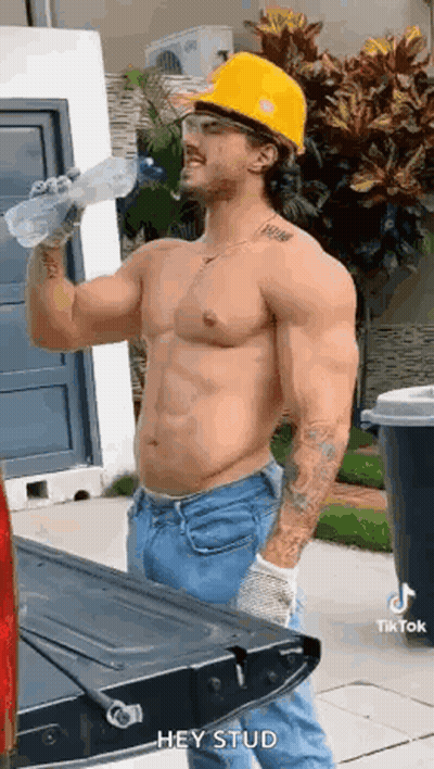 A Shirtless Construction Worker Is Drinking Water From A Bottle While Standing Next To A Truck . GIF