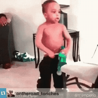 A Shirtless Little Boy Is Holding A Green Bottle In His Hand GIF