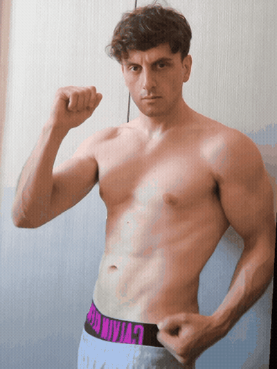 A Shirtless Man Flexes His Muscles In Front Of A Wall GIF