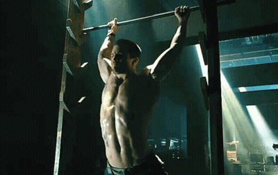 A Shirtless Man Hangs Upside Down On A Bar GIF