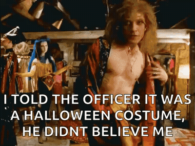 A Shirtless Man In A Halloween Costume Is Standing In Front Of A Woman In A Blue Dress . GIF