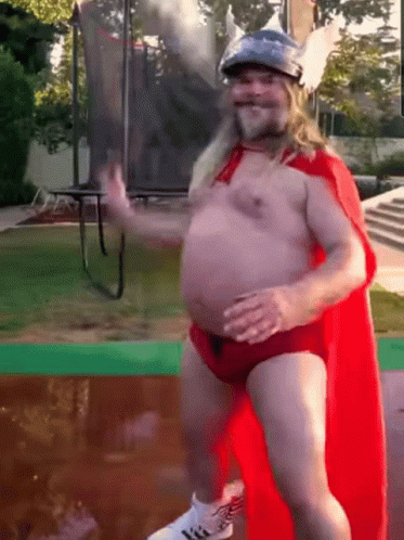 A Shirtless Man In A Red Cape And A Helmet Is Dancing In Front Of A Trampoline GIF