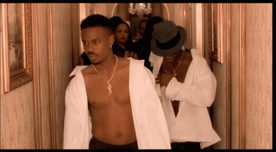 A Shirtless Man In A White Shirt Is Walking Down A Hallway With Other Men GIF