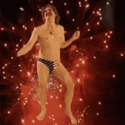 A Shirtless Man In An American Flag Underwear Is Dancing In Front Of A Fireworks Display . GIF