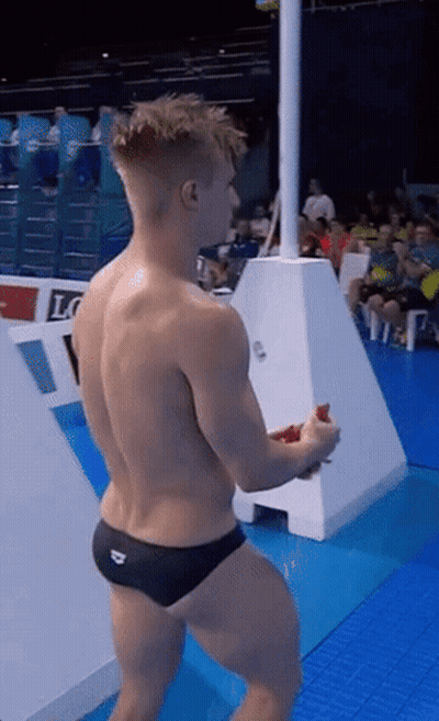 A Shirtless Man In Black Swim Trunks Stands On A Diving Board GIF