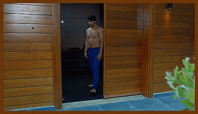 A Shirtless Man In Blue Pants Stands In The Doorway Of A Wooden House GIF