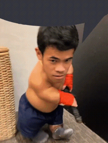 A Shirtless Man In Blue Shorts And Red Boxing Gloves Is Standing On A Wooden Floor GIF