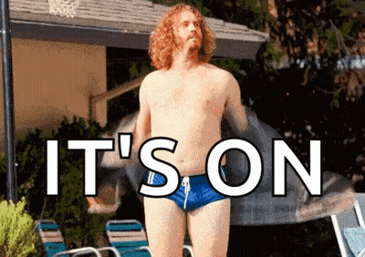 A Shirtless Man In Blue Swim Trunks Is Standing In Front Of A Pool With The Words " It 'S On " Above Him . GIF