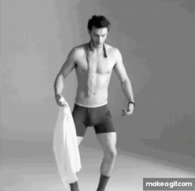 A Shirtless Man In Boxer Shorts And A Tie Is Holding A White Shirt In His Hand . GIF