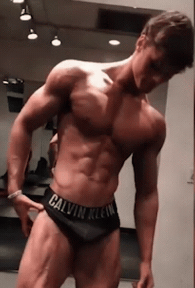 A Shirtless Man In Calvin Klein Underwear Is Standing In Front Of A Mirror In A Gym . GIF