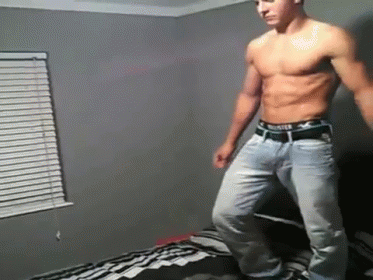 A Shirtless Man In Jeans Is Standing On A Bed . GIF
