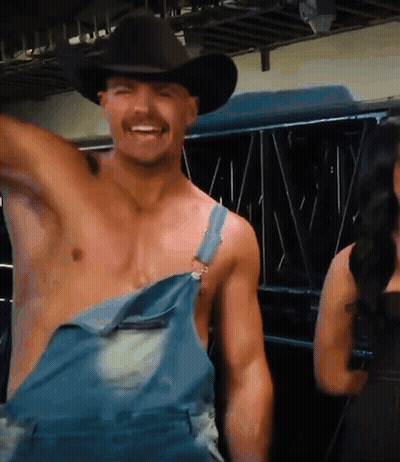 A Shirtless Man In Overalls And A Cowboy Hat Smiles GIF
