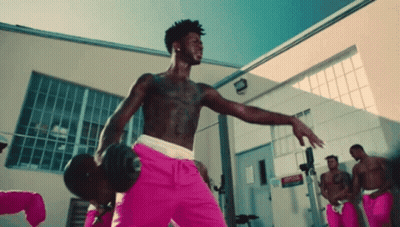 A Shirtless Man In Pink Shorts Is Holding A Dumbbell In A Gym GIF