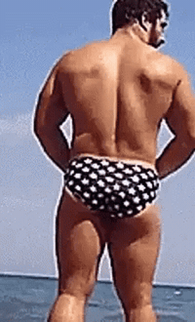 A Shirtless Man In Polka Dot Swim Trunks Is Standing In The Water . GIF