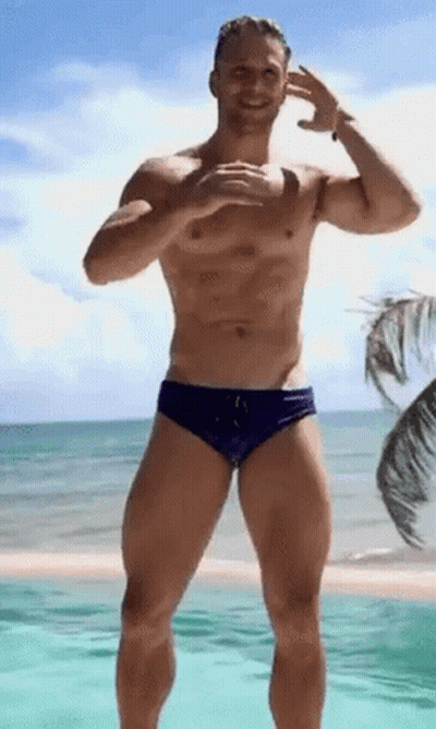 A Shirtless Man In Purple Swim Trunks Is Standing On A Beach . GIF