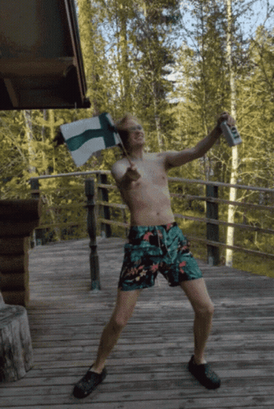 A Shirtless Man In Swim Trunks Is Holding A Flag And A Can Of Beer GIF