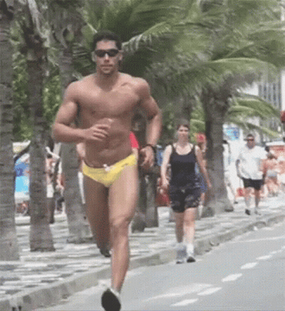 A Shirtless Man In Yellow Swim Trunks Is Running Down A Sidewalk GIF