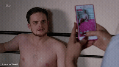 A Shirtless Man Is Being Photographed On A Cell Phone By Someone With Itv Written On The Bottom Of The Screen GIF