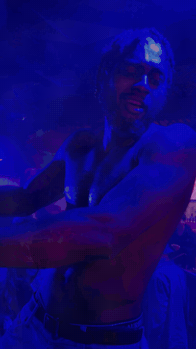 A Shirtless Man Is Dancing In A Dark Room With A Blue Light Behind Him GIF