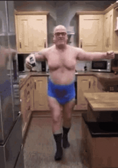 A Shirtless Man Is Dancing In A Kitchen While Holding A Bottle Of Beer . GIF
