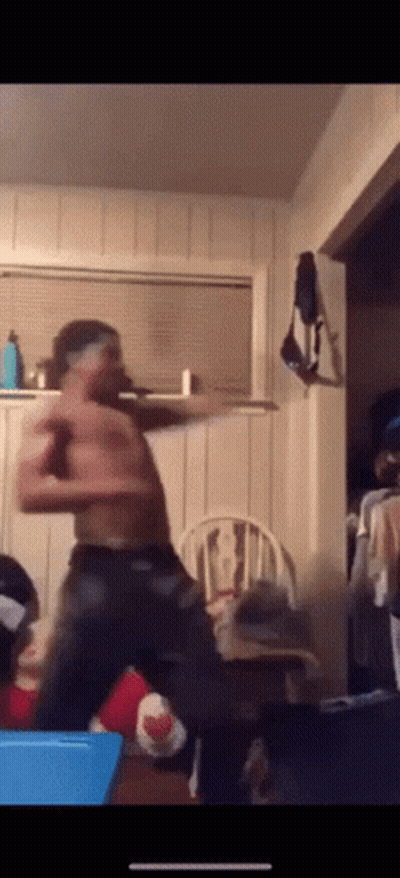 A Shirtless Man Is Dancing In A Living Room With A Chair In The Background GIF