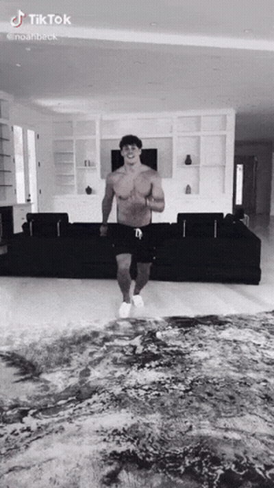 A Shirtless Man Is Dancing In A Living Room With A Couch . GIF