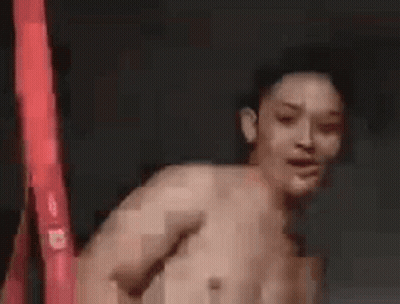A Shirtless Man Is Dancing In Front Of A Red Light . GIF
