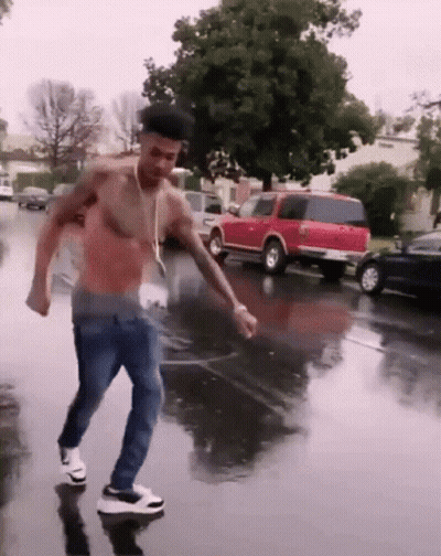 A Shirtless Man Is Dancing In The Rain On A Wet Street GIF