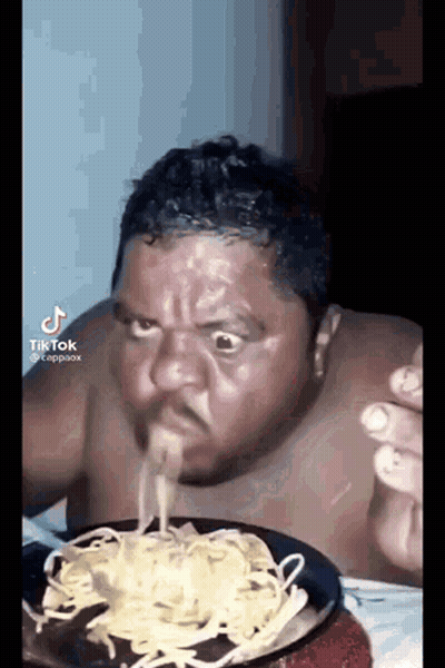 A Shirtless Man Is Eating A Plate Of Noodles With His Mouth Open . GIF