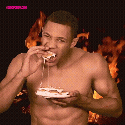 A Shirtless Man Is Eating A Sandwich With Flames In The Background And The Words Cosmopolitan.com Visible GIF