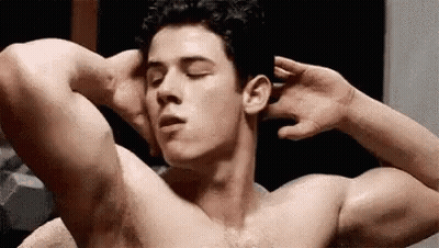 A Shirtless Man Is Flexing His Muscles In A Locker Room . GIF