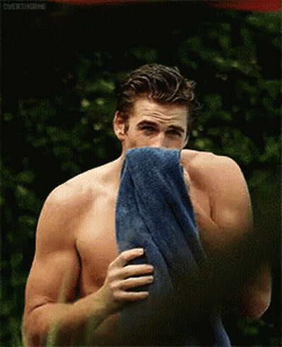 A Shirtless Man Is Holding A Blue Towel Over His Mouth GIF