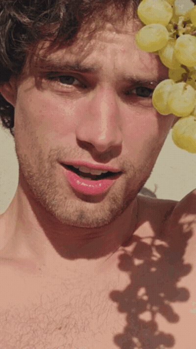 A Shirtless Man Is Holding A Bunch Of Grapes Over His Head GIF