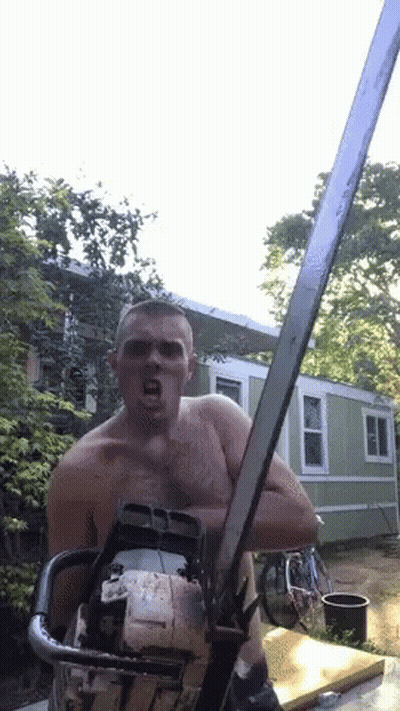 A Shirtless Man Is Holding A Chainsaw In Front Of A House GIF
