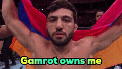 A Shirtless Man Is Holding A Colorful Flag With The Words Gamrot Owns Me Above Him GIF